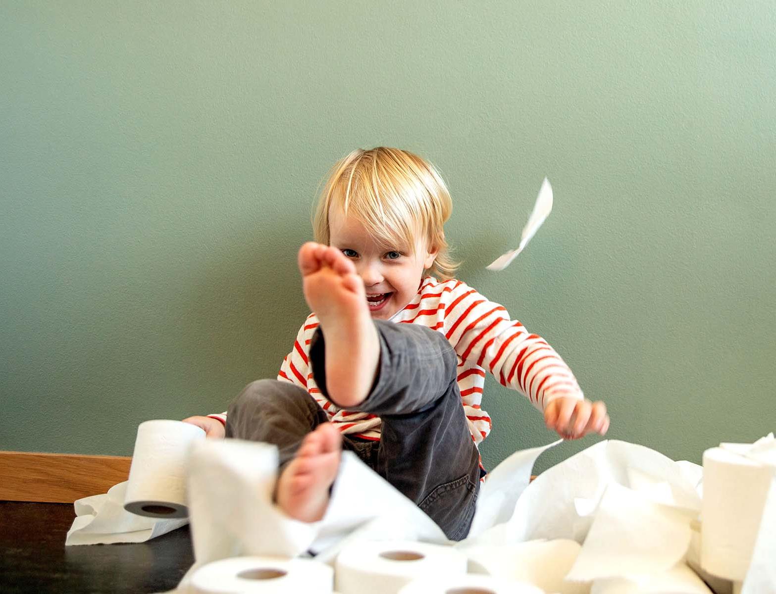 A toddler gleefully throwing toilet paper around.